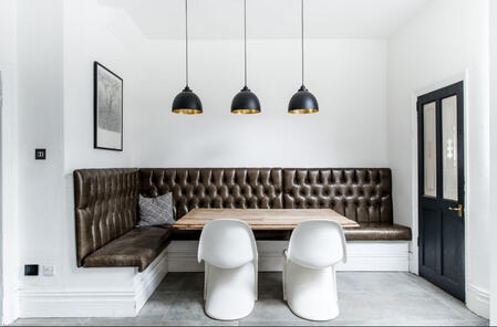 A stylish dining nook featuring a tufted leather banquette, rustic wooden table, sleek white chairs, and black pendant lights, showcasing a perfect blend of modern and classic commercial furniture design.